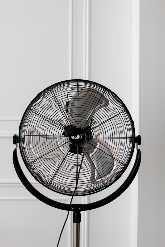 Black stand fan with industrial design against a white wall, offering modern home cooling solutions.